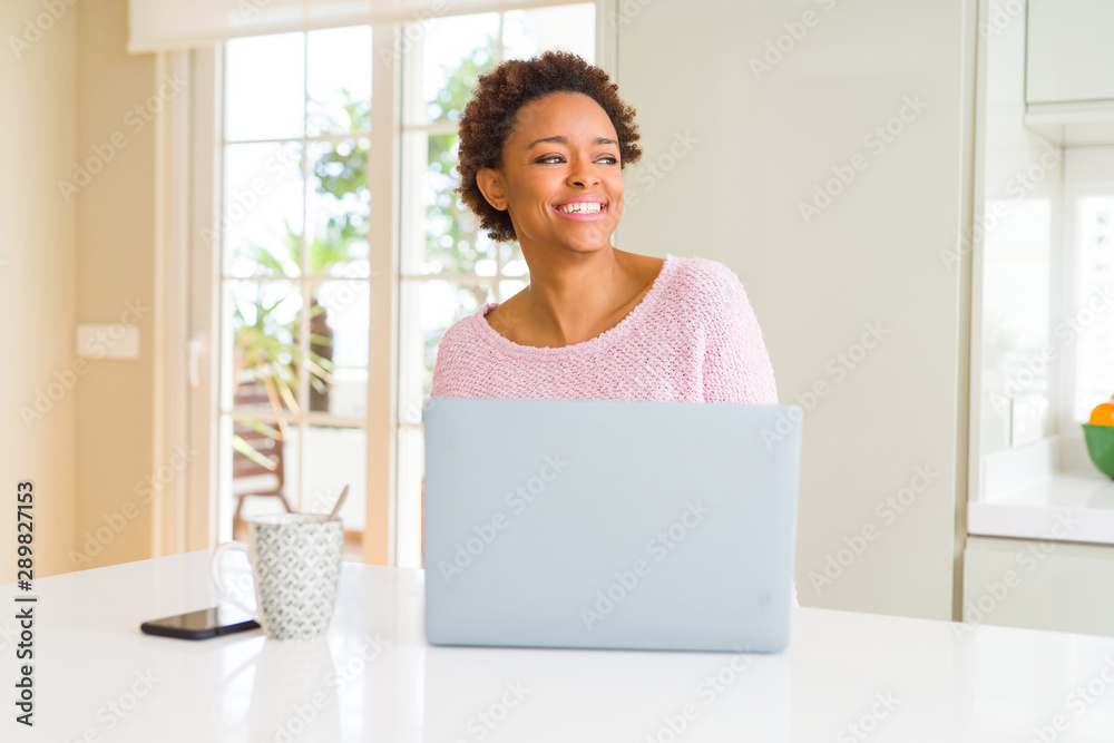 Young african american woman working using computer laptop looking away to side with smile on face, natural expression. Laughing confident. Young african american woman working using computer laptop looking away to side with smile on face, natural expression. Laughing confident.