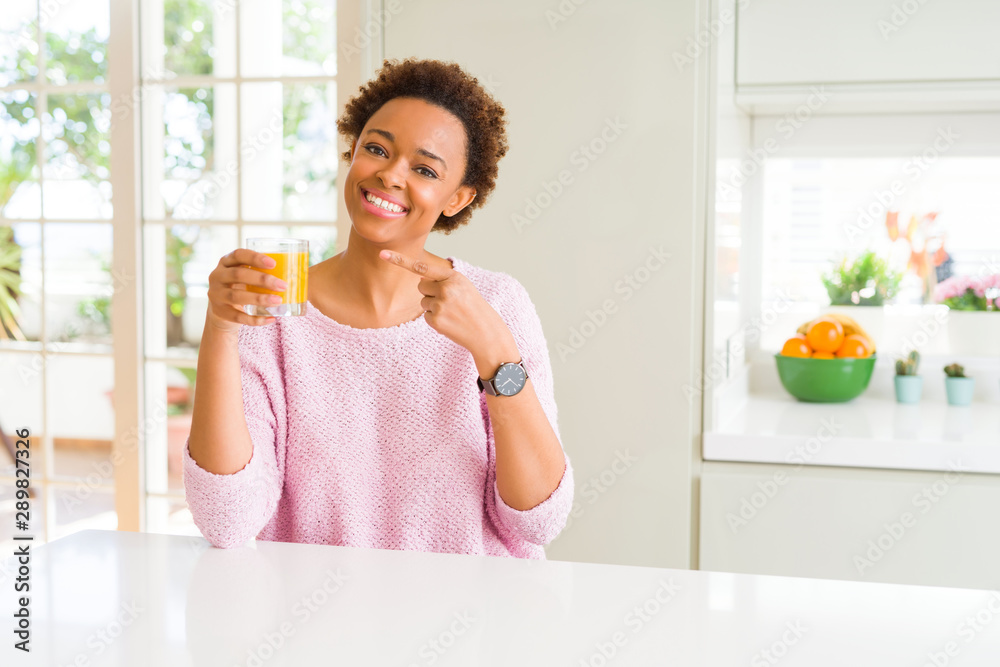 Young african american woman driking orange juice at home very happy pointing with hand and finger Young african american woman driking orange juice at home very happy pointing with hand and finger