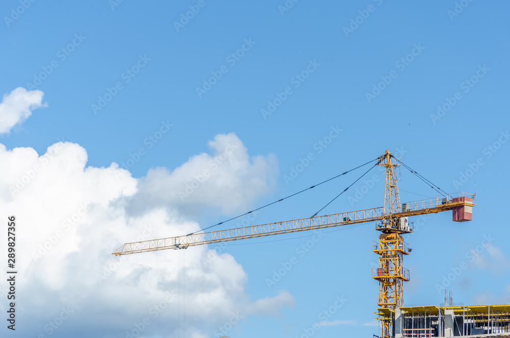 The construction of a multistory building against the blue sky, stands next to a yellow tower crane. Photo bottom up