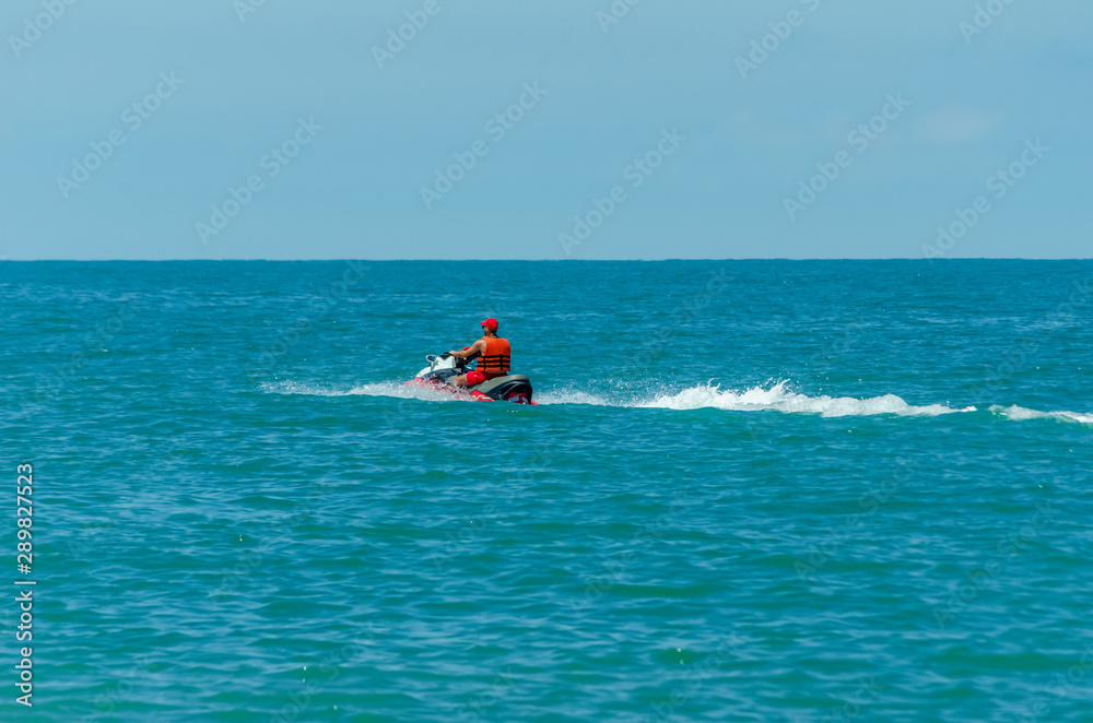 lifeguard in an orange vest on a water scooter cuts the waves along the black sea near the coast in sunny weather