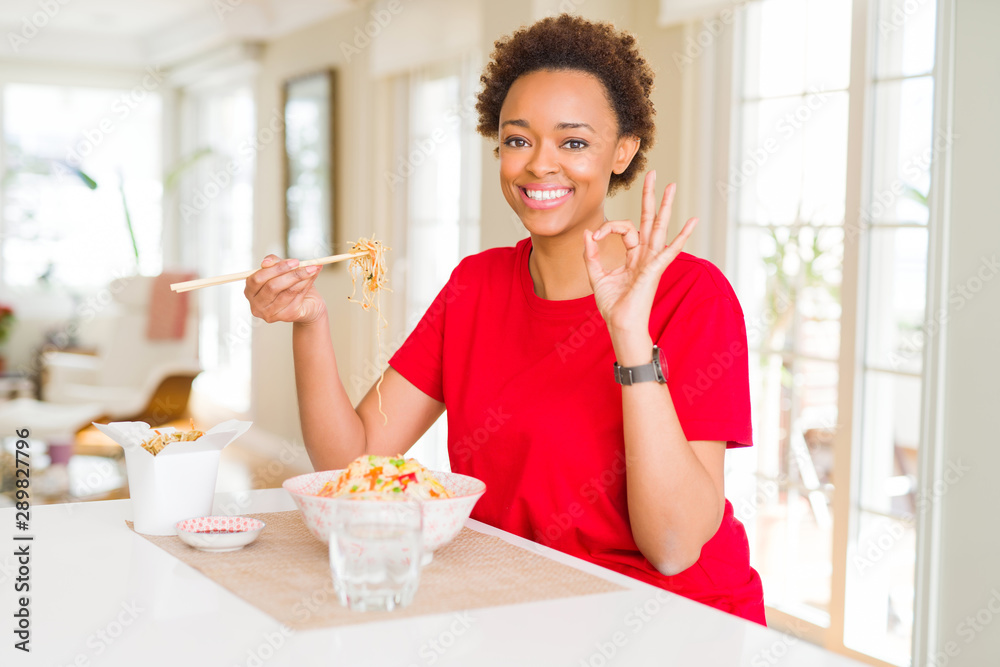 Young african american woman with afro hair eating asian food at home doing ok sign with fingers, excellent symbol Young african american woman with afro hair eating asian food at home doing ok sign with fingers, excellent symbol