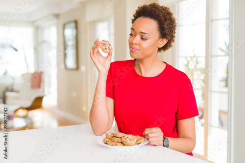 Young african american woman eating chocolate chips cookies with a confident expression on smart face thinking serious