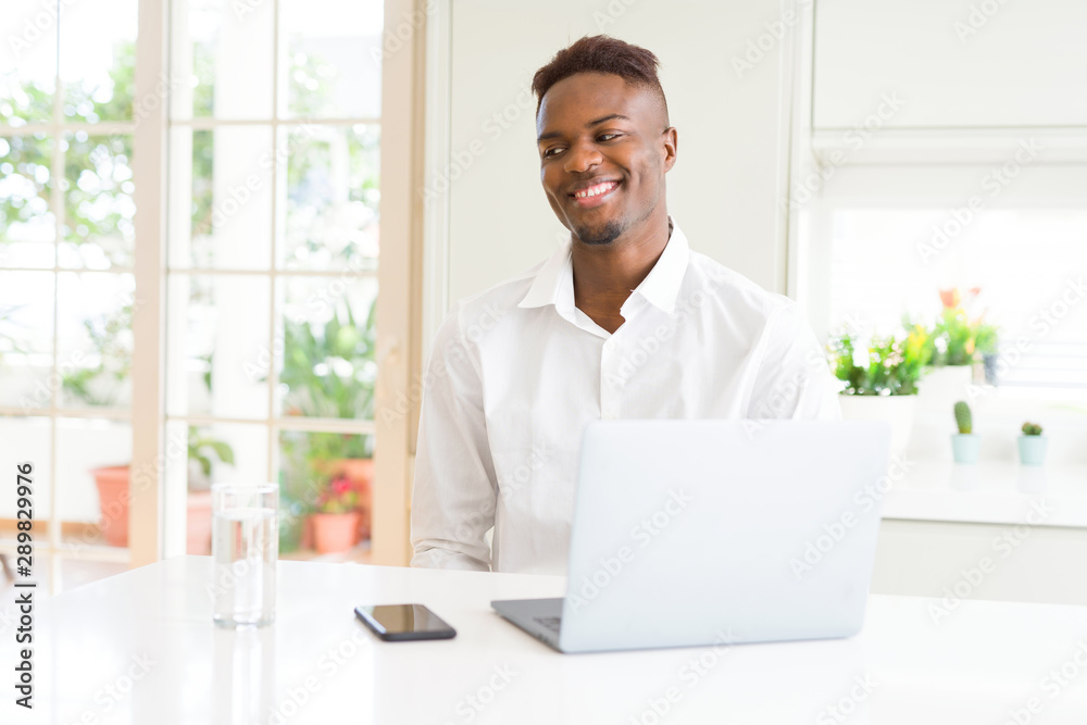 African american business man working using laptop looking away to side with smile on face, natural expression. Laughing confident.