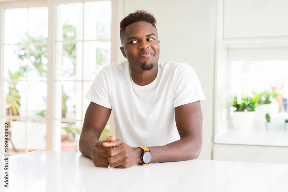 Handsome african american man on white table at home smiling looking side and staring away thinking. Handsome african american man on white table at home smiling looking side and staring away thinking.