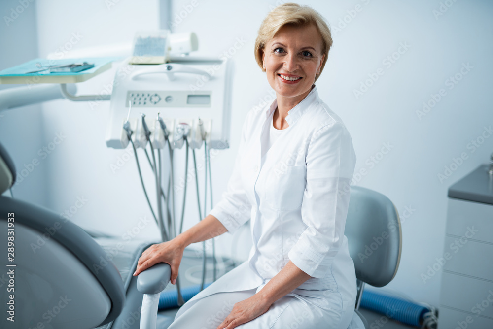 Obraz premium Smiling doctor is sitting in dental clinic