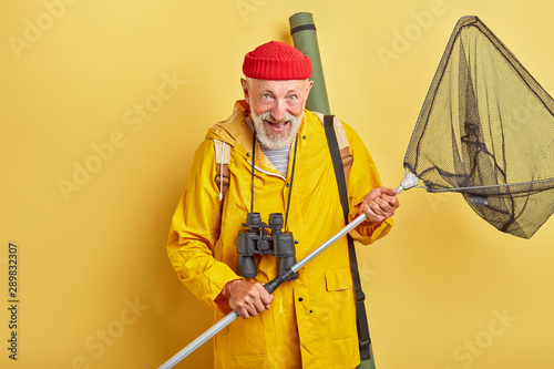 man is crazy about fishing . positive feeling and emotion. necessary equipment. professional fishman with binocular and equipment going to river. close up photo. isolated yellow background photo