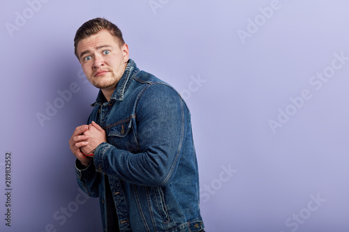 young emotional muscular man in denim jacket standing with fearful expression,man is being afraid of spiders, mice. close up side view photo. sale, discount, copy space photo