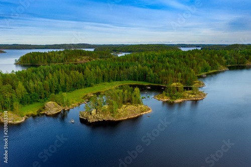 Aerial view of of small islands on a blue lake Saimaa. Landscape with drone. Blue lakes  islands and green forests from above on a cloudy summer day. Lake landscape in Finland.