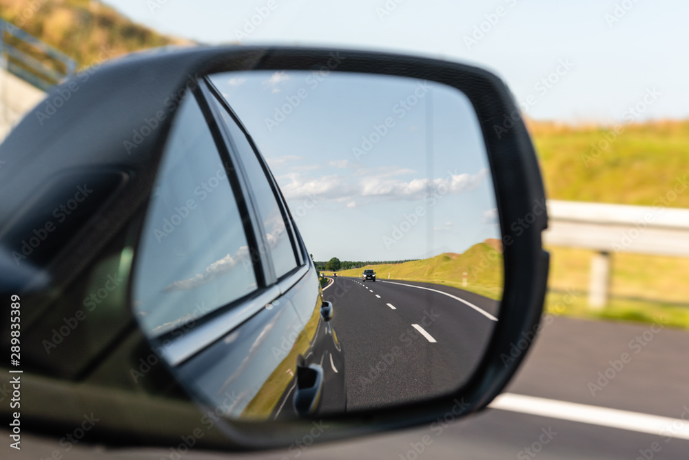 Asphalt road with vehicle reflected in car mirror. Concept of safe driving.