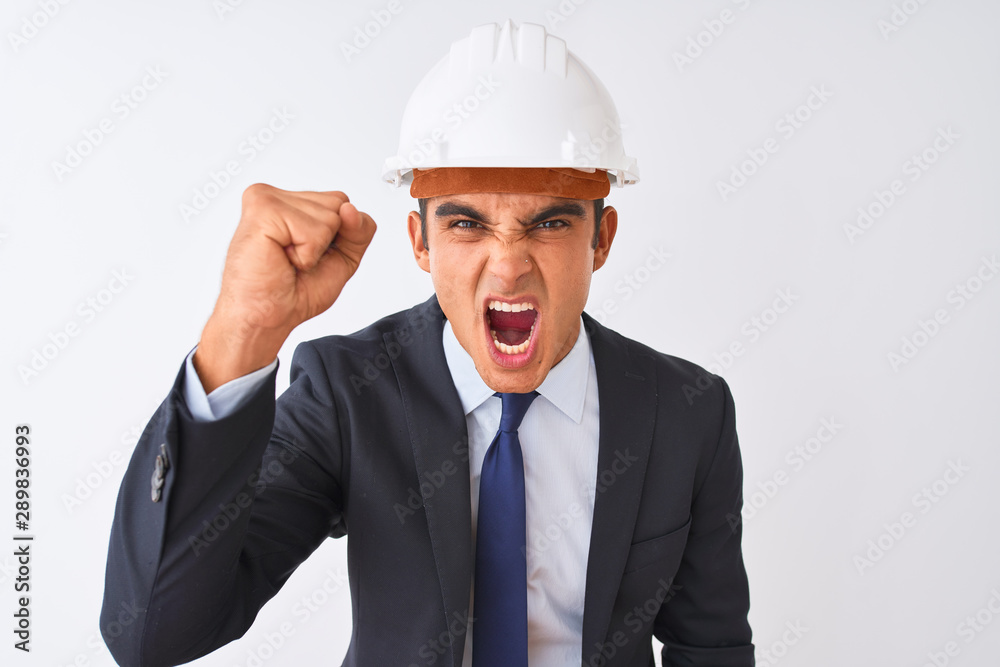Young handsome architect man wearing suit and helmet over isolated white background angry and mad raising fist frustrated and furious while shouting with anger. Rage and aggressive concept. Young handsome architect man wearing suit and helmet over isolated white background angry and mad raising fist frustrated and furious while shouting with anger. Rage and aggressive concept.