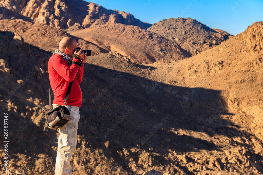 Young man taking a photos of mountain range Red Sea Hills in Arabian desert, Egypt
