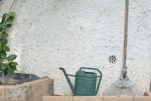 Watercan and rake against a white wall