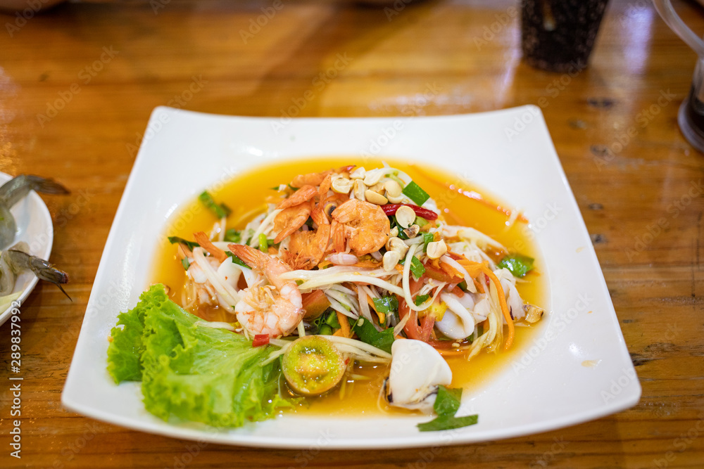 Hot and spicy seafood papaya salad in white ceramic plate on wooden table Hot and spicy seafood papaya salad in white ceramic plate on wooden table