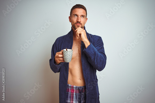 Shirtless man wearing comfortable pajamas and robe drinking cup of coffee serious face thinking about question, very confused idea