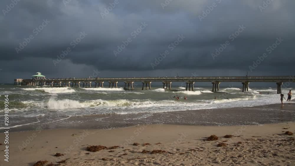 North Side of Deerfield Beach, Florida Pier in a Sunny Late Afternoon with a Dark Gray Cloudy Sky, Rough Seas with White Caps and Sand Below North Side of Deerfield Beach, Florida Pier in a Sunny Late Afternoon with a Dark Gray Cloudy Sky, Rough Seas with White Caps and Sand Below