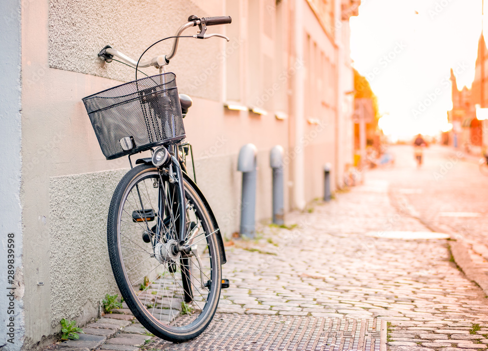 Black bicycle with shopping basket stand near the wall on the street, sunlight on the background, horizontal