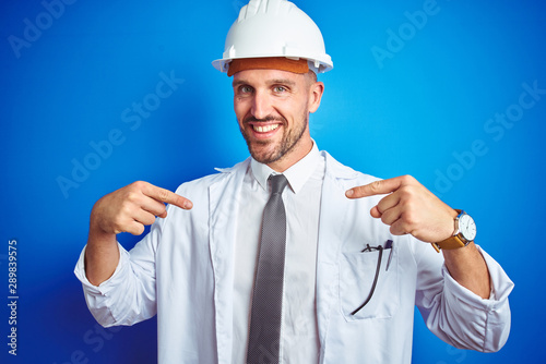 Young handsome engineer man wearing safety helmet over blue isolated background looking confident with smile on face, pointing oneself with fingers proud and happy.
