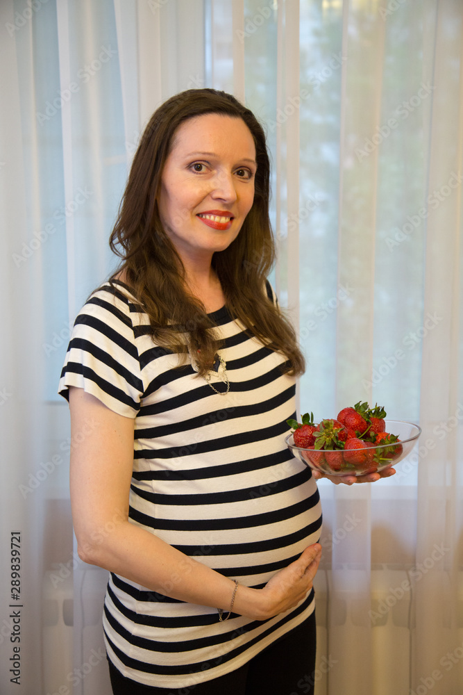pregnancy, motherhood, the concept of waiting-close - up of a happy pregnant woman with a big belly in a window with strawberries.