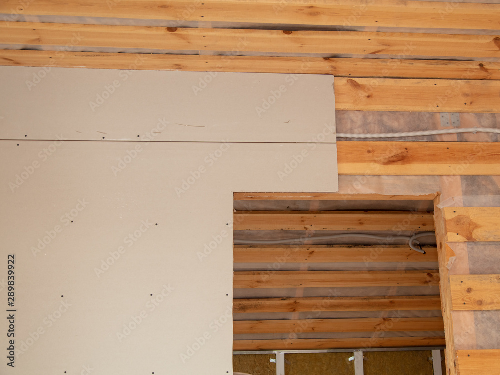A worker fastens a sheet of drywall to the wall A worker fastens a sheet of drywall to the wall