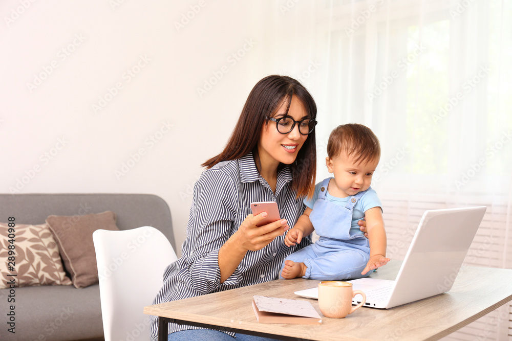 Stay at home mom working remotely on laptop while taking care of her baby. Young mother on maternity leave trying to freelance by the desk with toddler child. Close up, copy space, background. Stay at home mom working remotely on laptop while taking care of her baby. Young mother on maternity leave trying to freelance by the desk with toddler child. Close up, copy space, background.