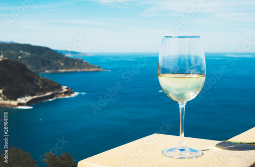 Drink glass white wine stand on background blue sea top view city coast from observation deck, romantic lonely toast with alcohol panoramic cityscape downtown, spain san sebastian vacation travel