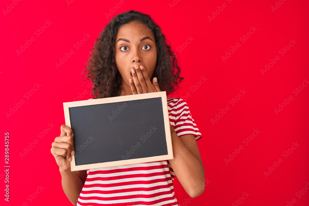 Young brazilian student woman holding blackboard standing over isolated red background cover mouth with hand shocked with shame for mistake, expression of fear, scared in silence, secret concept Young brazilian student woman holding blackboard standing over isolated red background cover mouth with hand shocked with shame for mistake, expression of fear, scared in silence, secret concept