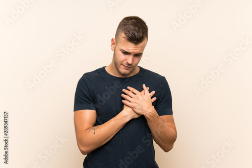 Young handsome blonde man over isolated background having a pain in the heart