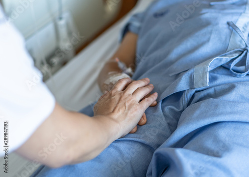 Elderly senior patient (ageing old adult person) lying in hospital bed with family caregiver or caretaker nurse in nursing hospice, geriatrician palliative home having medical health care service