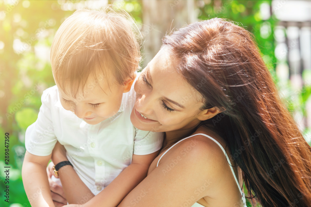 Close up portrait of young woman and 4-year-old boy having fun. Mother is holding son in his arms and smiling. Greenery in the background. Mom and son concept. Horizontal shot. Front view Close up portrait of young woman and 4-year-old boy having fun. Mother is holding son in his arms and smiling. Greenery in the background. Mom and son concept. Horizontal shot. Front view