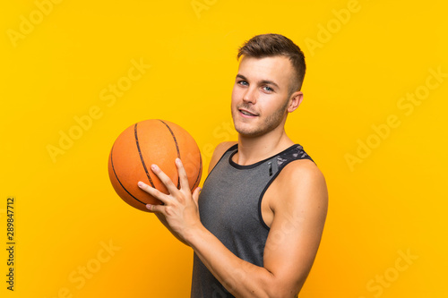 Young handsome blonde man holding a basket ball over isolated yellow background
