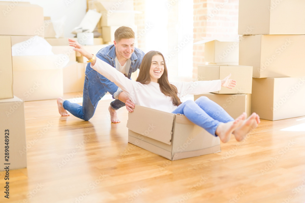 Beautiful young couple smiling in love having fun riding inside a cardboard box, celebrating moving to a new home