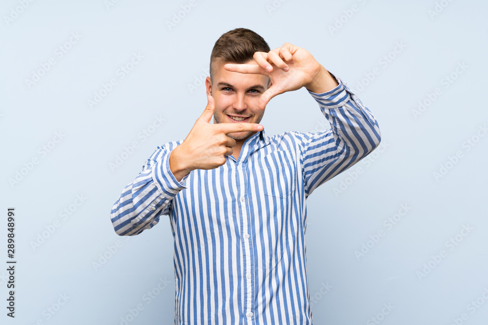 Young handsome blonde man over isolated blue background focusing face. Framing symbol Young handsome blonde man over isolated blue background focusing face. Framing symbol