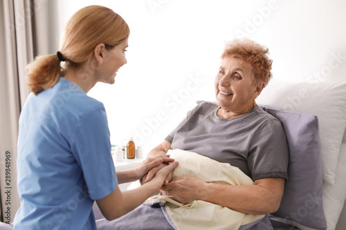 Nurse assisting elderly woman in bed indoors © New Africa