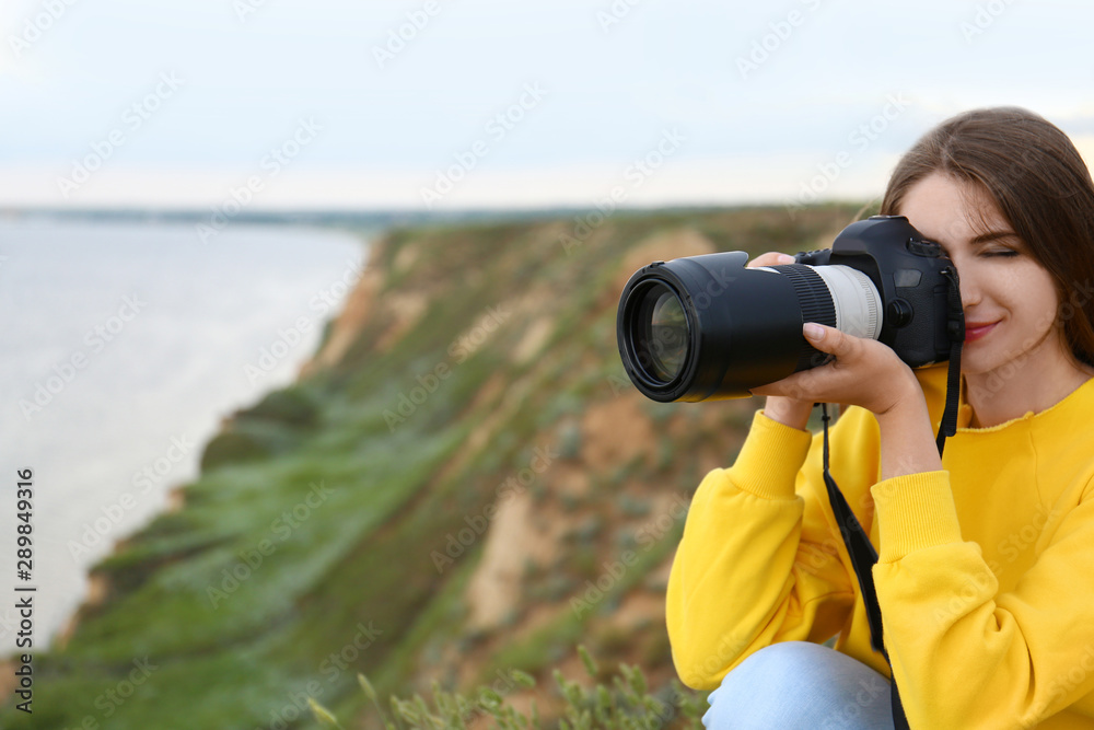 Obraz premium Female photographer taking picture of beautiful landscape with professional camera on green hill. Space for text