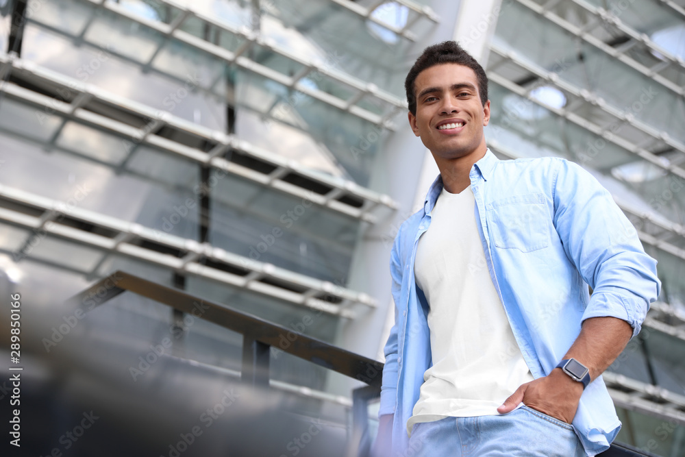 Handsome young African-American man on city street, low angle view. Space for text Handsome young African-American man on city street, low angle view. Space for text