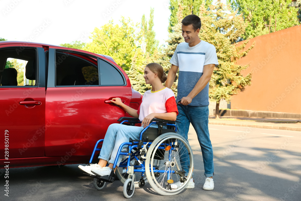 Young man helping disabled woman in wheelchair to get into car outdoors Young man helping disabled woman in wheelchair to get into car outdoors