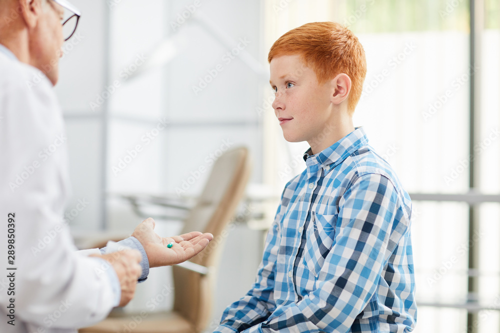 Fototapeta premium Portrait of smiling teenage boy looking at doctor during consultation in child clinic or hospital, copy space