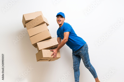 Delivery man over isolated white wall with lots boxes and stumbling