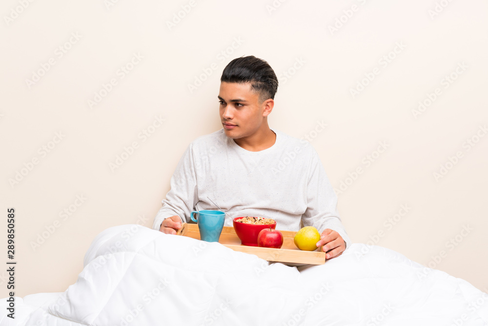 Young man having breakfast in bed looking side Young man having breakfast in bed looking side