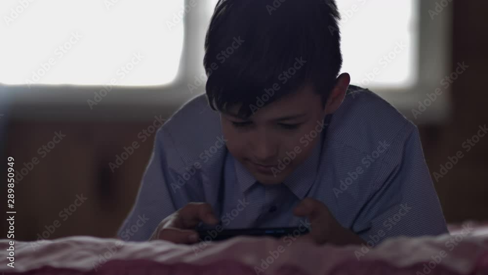 boy lies on the bed at home and uses a phone in the evening, plays games on the phone boy lies on the bed at home and uses a phone in the evening, plays games on the phone