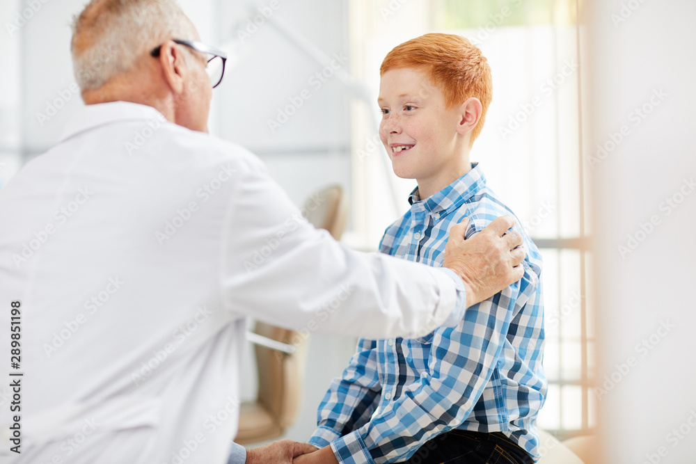 Portrait of little boy in doctors office smiling happily during consultation with senior physician in child clinic, copy space Portrait of little boy in doctors office smiling happily during consultation with senior physician in child clinic, copy space
