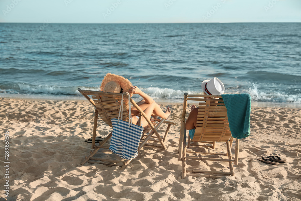 Young couple relaxing in deck chairs on beach near sea Young couple relaxing in deck chairs on beach near sea