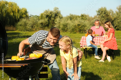 Father with little girl at barbecue grill and their family in park
