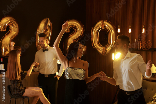 Young people celebrating New Year in club. Golden 2020 balloons on background