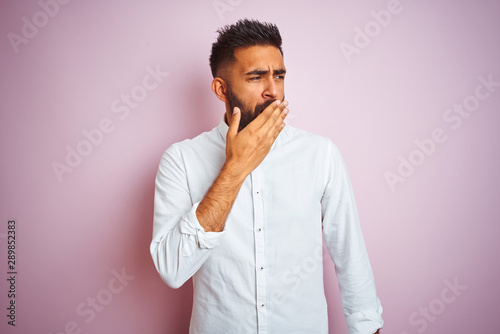 Young indian businessman wearing elegant shirt standing over isolated pink background bored yawning tired covering mouth with hand. Restless and sleepiness.