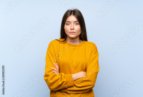 Caucasian young woman over isolated blue wall keeping arms crossed