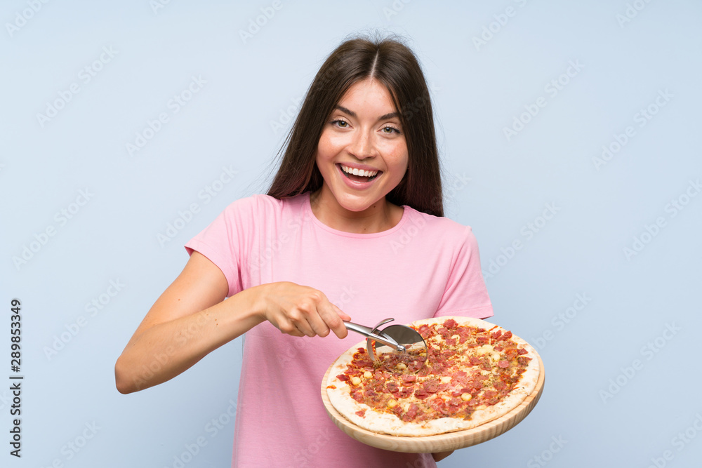 Pretty young girl holding a pizza over isolated blue wall Pretty young girl holding a pizza over isolated blue wall
