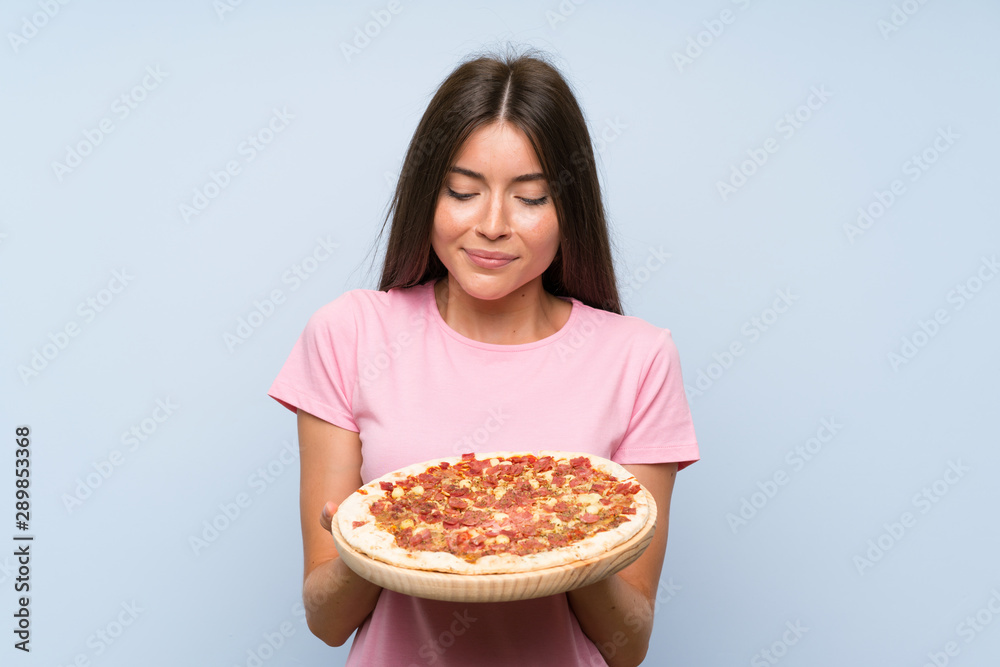 Pretty young girl holding a pizza over isolated blue wall Pretty young girl holding a pizza over isolated blue wall