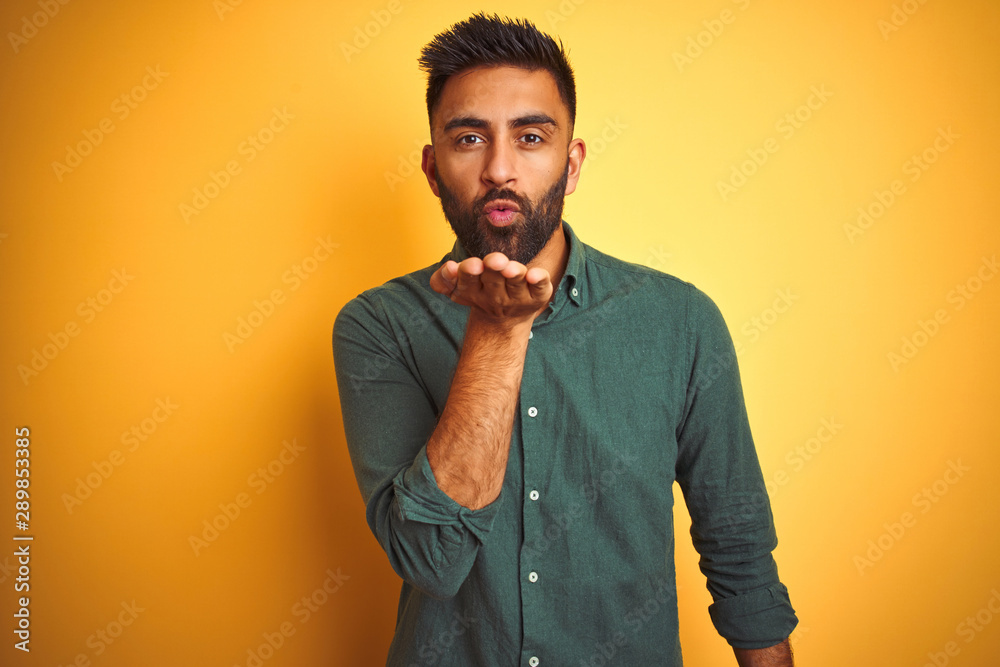 Young indian businessman wearing elegant shirt standing over isolated white background looking at the camera blowing a kiss with hand on air being lovely and sexy. Love expression. Young indian businessman wearing elegant shirt standing over isolated white background looking at the camera blowing a kiss with hand on air being lovely and sexy. Love expression.