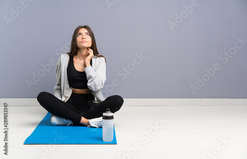 Young sport woman sitting on the floor with mat thinking an idea